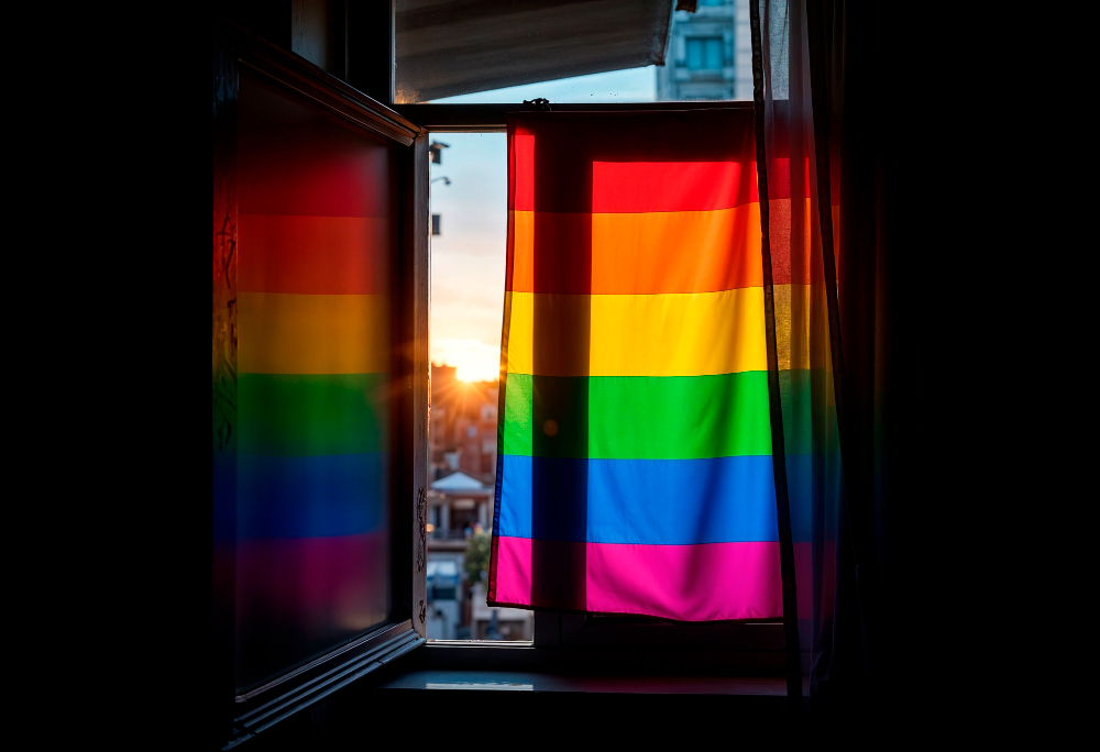 Uma bandeira lgbt+ estendida na janela. A imagem representa maneiras criativas de se assumir para a família.